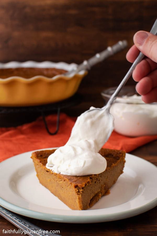 A slice of pumpkin pie getting a dollop of whipped cream