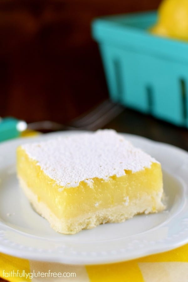 A plate with a big, beautiful piece of gluten free Lemon Bars with a thick layer of lemon curd and sprinkled with powdered sugar on top.