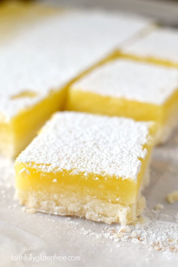 A plate with a big, beautiful piece of gluten free Lemon Bars with a thick layer of lemon curd and sprinkled with powdered sugar on top.