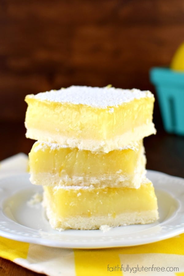 A plate with a big, beautiful piece of gluten free Lemon Bars with a thick layer of lemon curd and sprinkled with powdered sugar on top.
