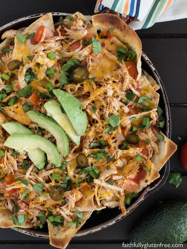 A skillet full of chicken nachos, topped with salsa, cheese, peppers, and sliced avocado.
