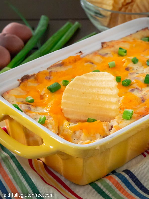 A dish filled with loaded baked potato dip with a chip standing upright in the dip.