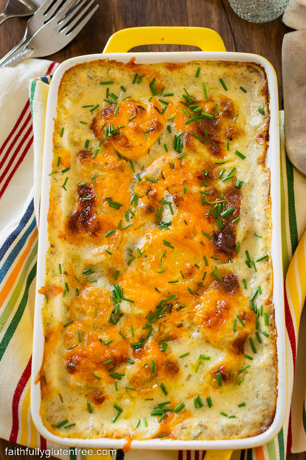 a baking dish with cheese covered scalloped potatoes, sprinkled with chopped chives