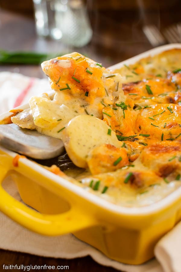 A spoon of scalloped potatoes being served from a baking dish