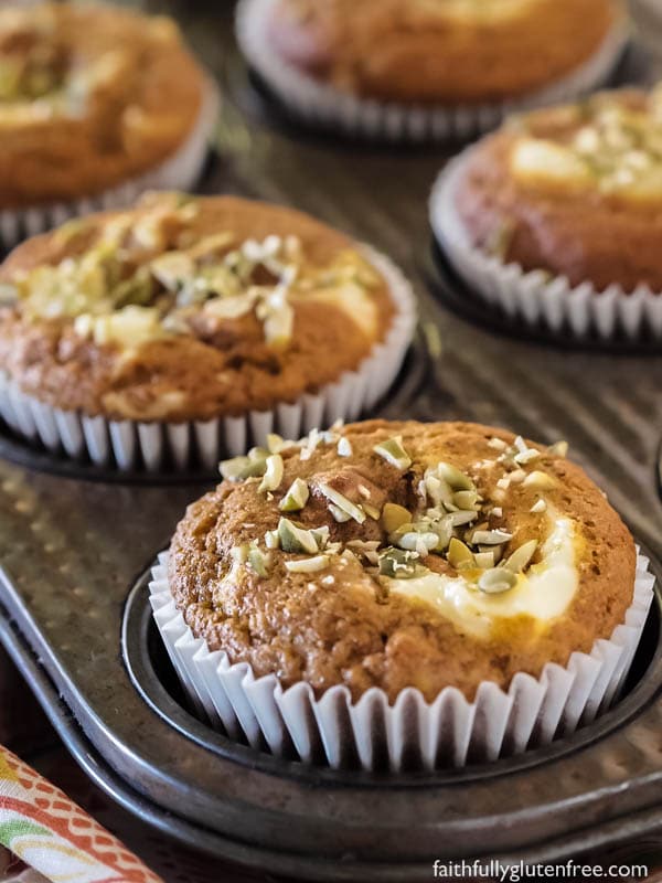 A muffin tin of gluten free pumpkin cream cheese muffins topped with pumpkin seeds